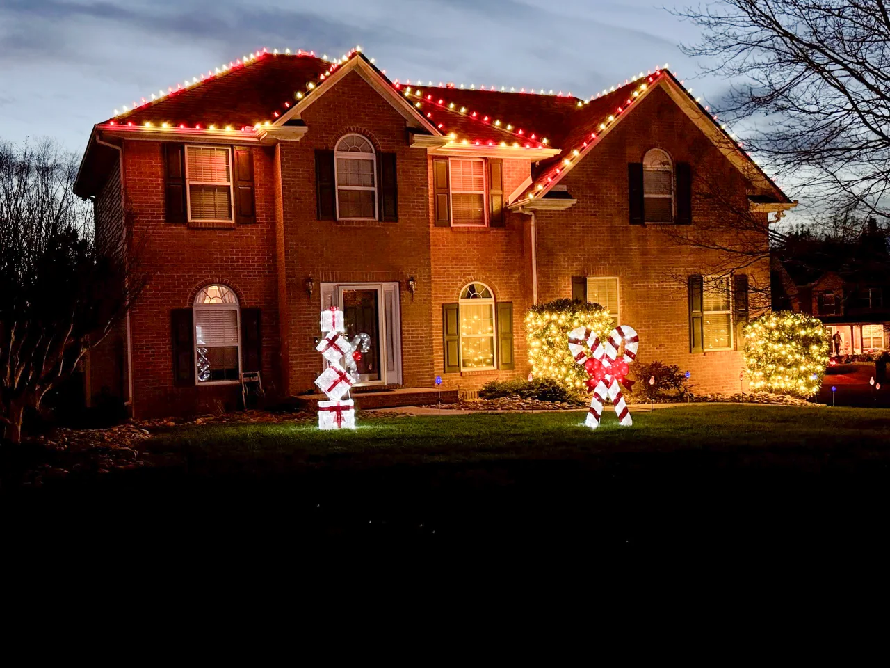 Two-story brick home with festive roofline lights, illuminated shrubs and candy cane decorations