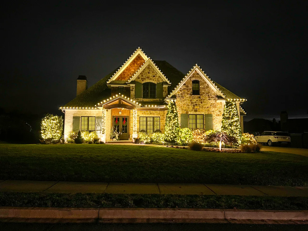 Warm-white roofline and landscape lights on a stone home at night